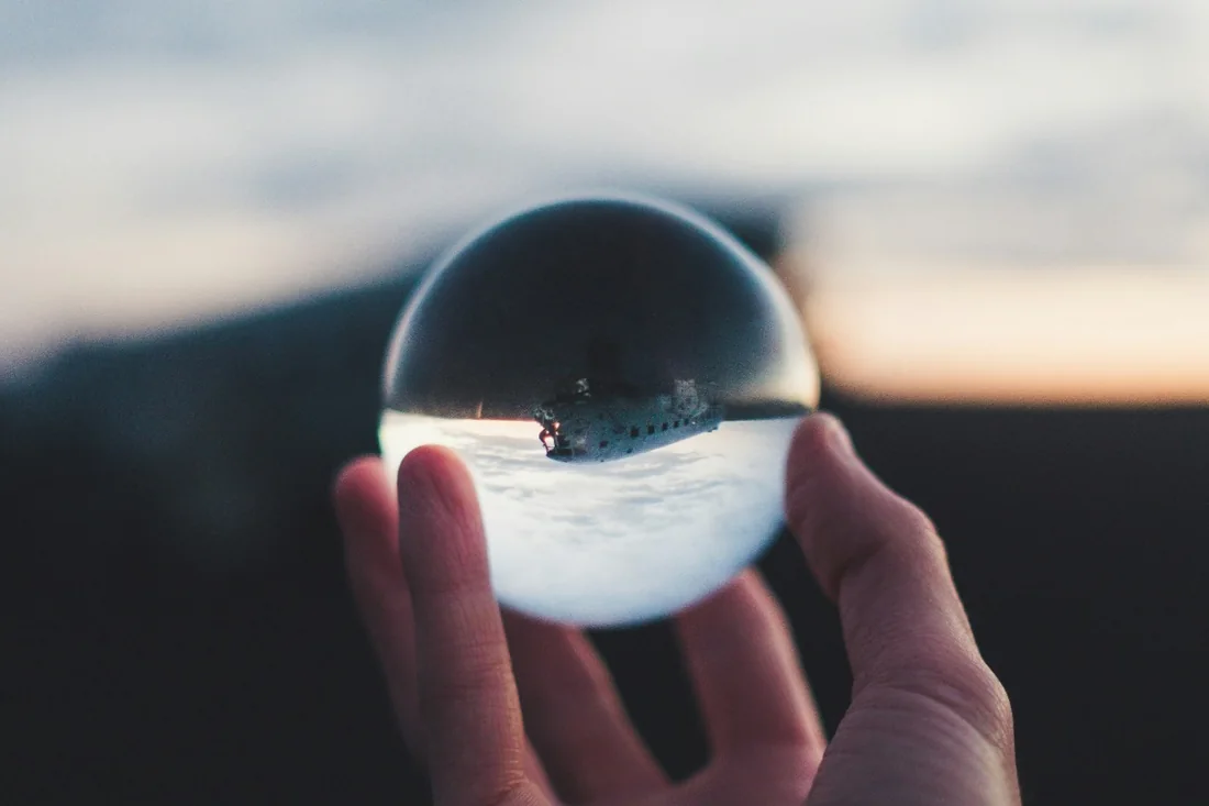 Una mano regge una sfera di vetro in cui si riflette capovolto un paesaggio al tramonto