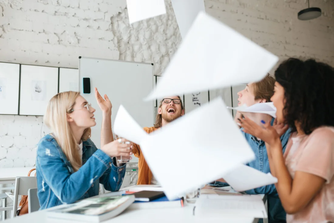 I collaboratori di AB Lavoro attorno al tavolo di una sala riunioni, sorridenti, mentre lanciano in aria dei fogli